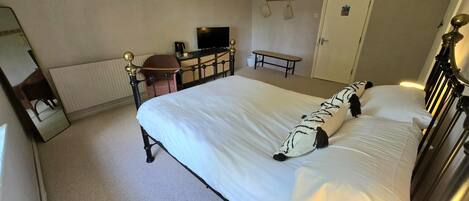 A hotel room with a large bed, a desk with a chair, a television, and a door.