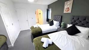 Quarto de hotel com duas camas, carpete cinza, parede de destaque verde e uma obra de arte emoldurada.