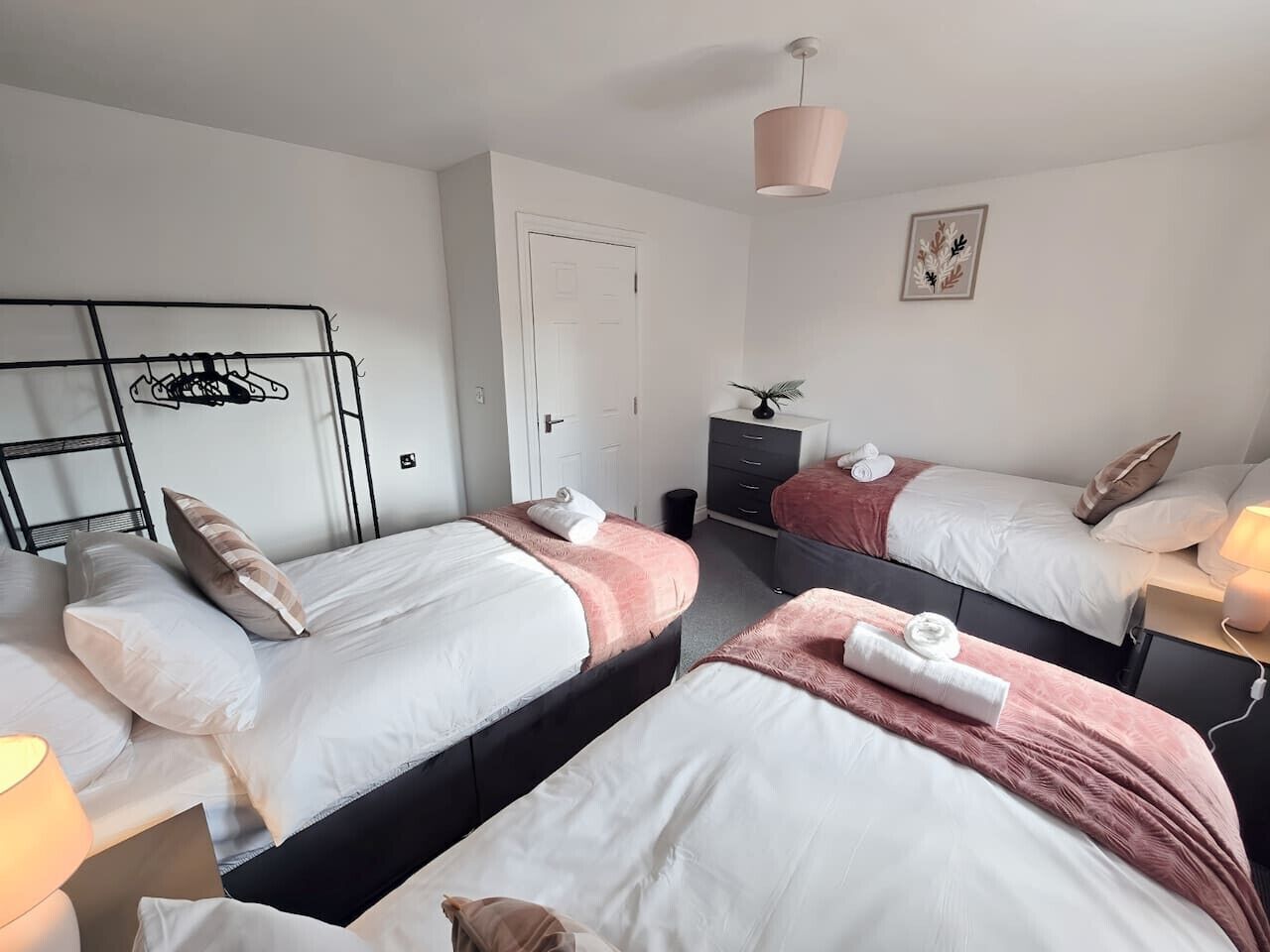 A hotel room with two beds, a wardrobe, a desk, and a hanging light fixture.