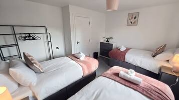 A hotel room with two beds, a wardrobe, a desk, and a hanging light fixture.