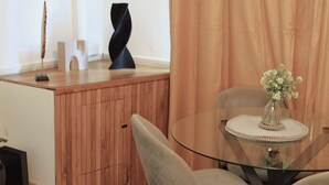 Un comedor con mesa de vidrio, sillas color beige, un jarrón con flores y un armario de madera.