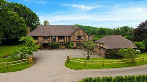 A traditional Tudor-style house with a central entrance, surrounded by a well-maintained lawn and a wooden fence.