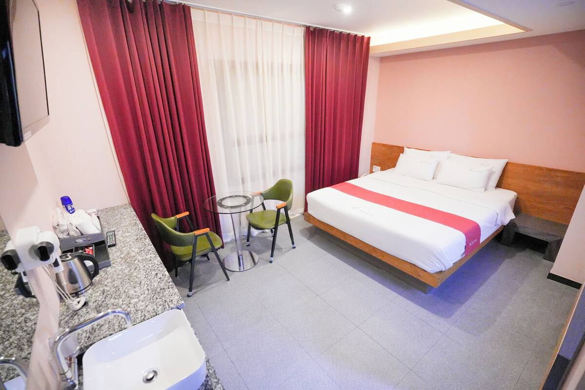 A hotel room with a bed, a small table with two chairs, a sink, and a mirror.