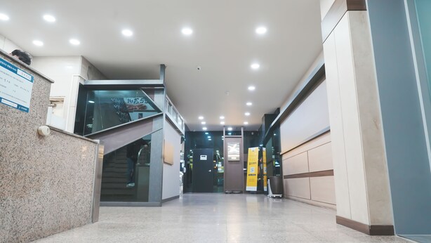 Un interior moderno con una escalera de cristal, un mostrador de recepción y un pasillo luminoso y ordenado.