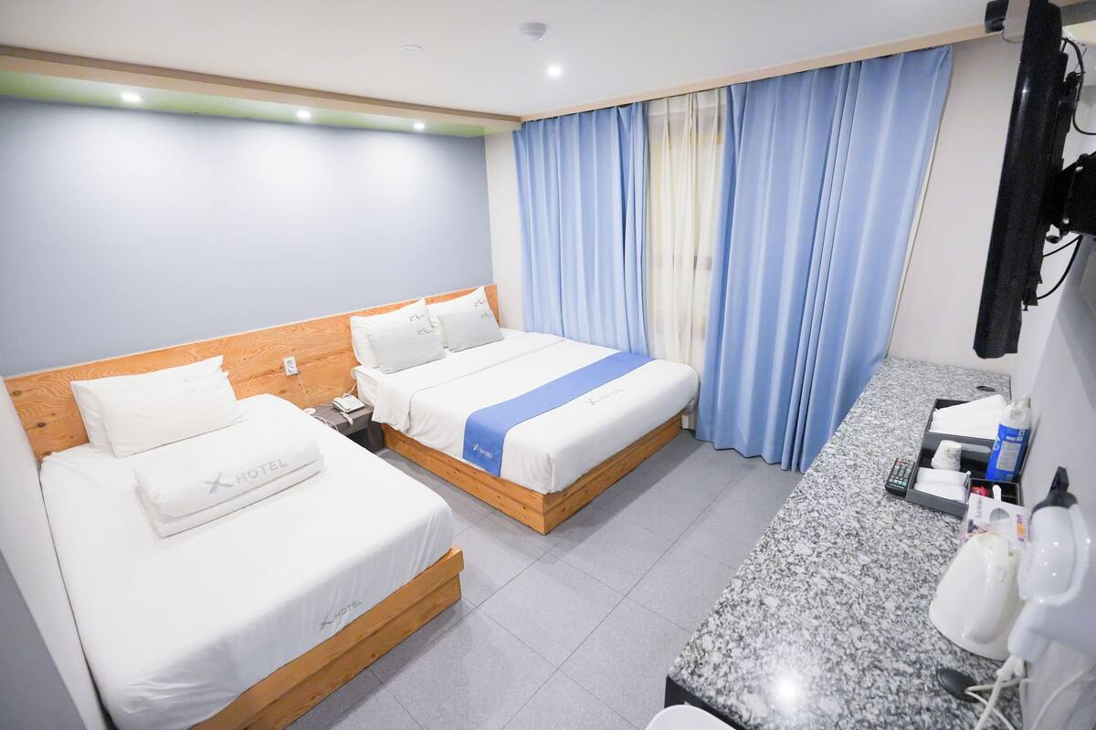 A hotel room with two beds, a wooden headboard, a marble countertop, a sink, and a mirror.