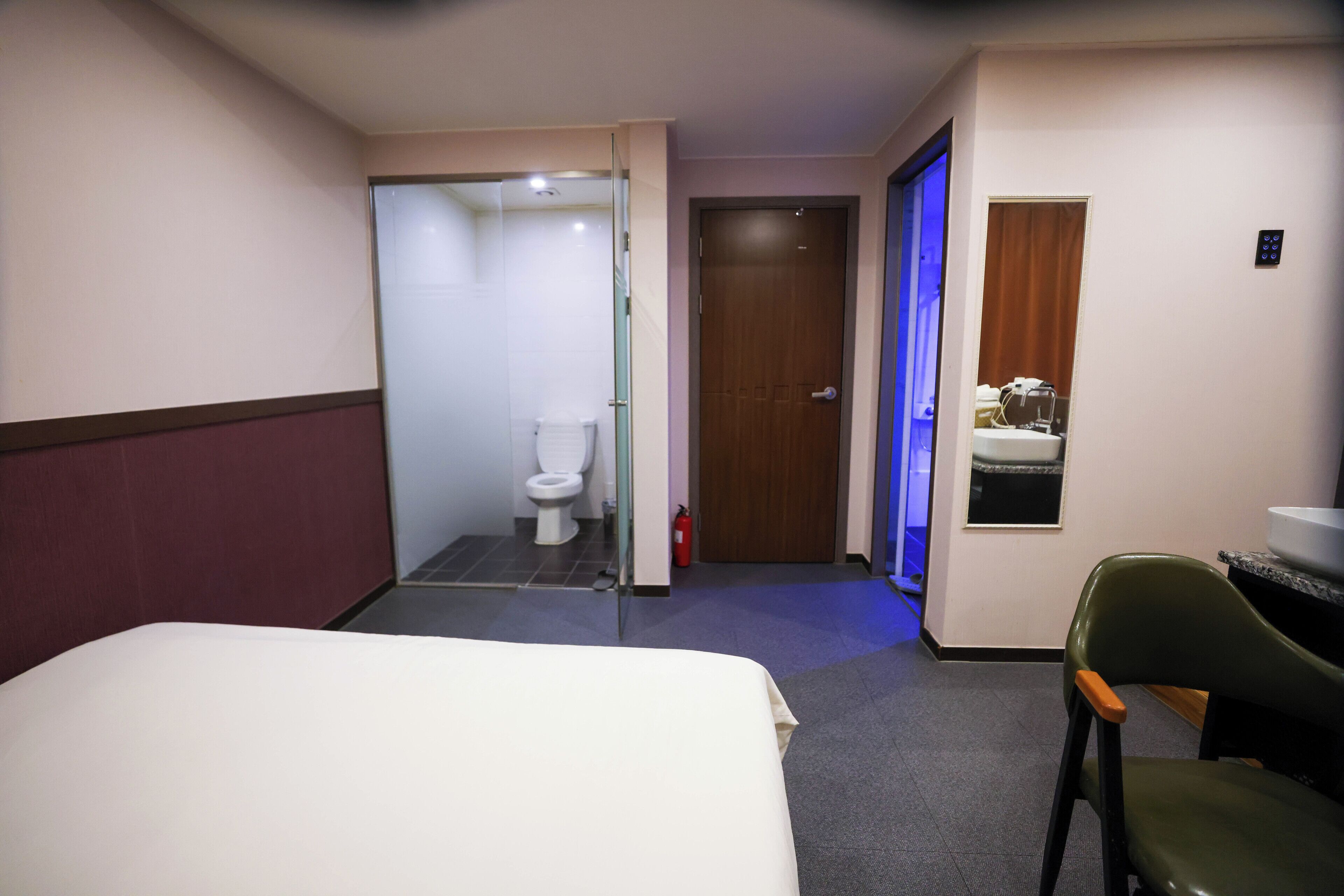 Une chambre d’hôtel avec un lit, une chaise, une salle de bain avec des toilettes et une petite fenêtre.