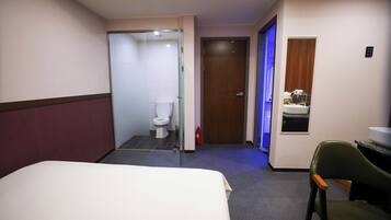 Une chambre d’hôtel avec un lit, une chaise, une salle de bain avec des toilettes et une petite fenêtre.