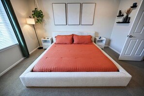 Une chambre à coucher avec un grand lit, deux tables de chevet, une commode, une lampe, une plante et une porte.