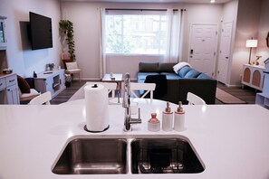 A modern kitchen with a central island, stainless steel sink, and a dining area with a table and chairs.