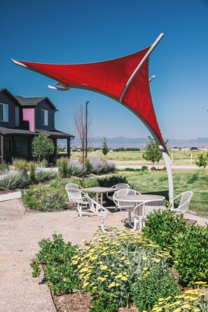 Un patio con mobiliario exterior, un toldo rojo y una casa al fondo.