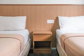 Une chambre d’hôtel avec deux lits simples, une tête de lit en bois, une table de chevet et une prise de courant.