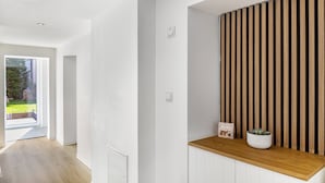 Un interior moderno con un banco de madera, una planta en maceta y una pared blanca con listones verticales.