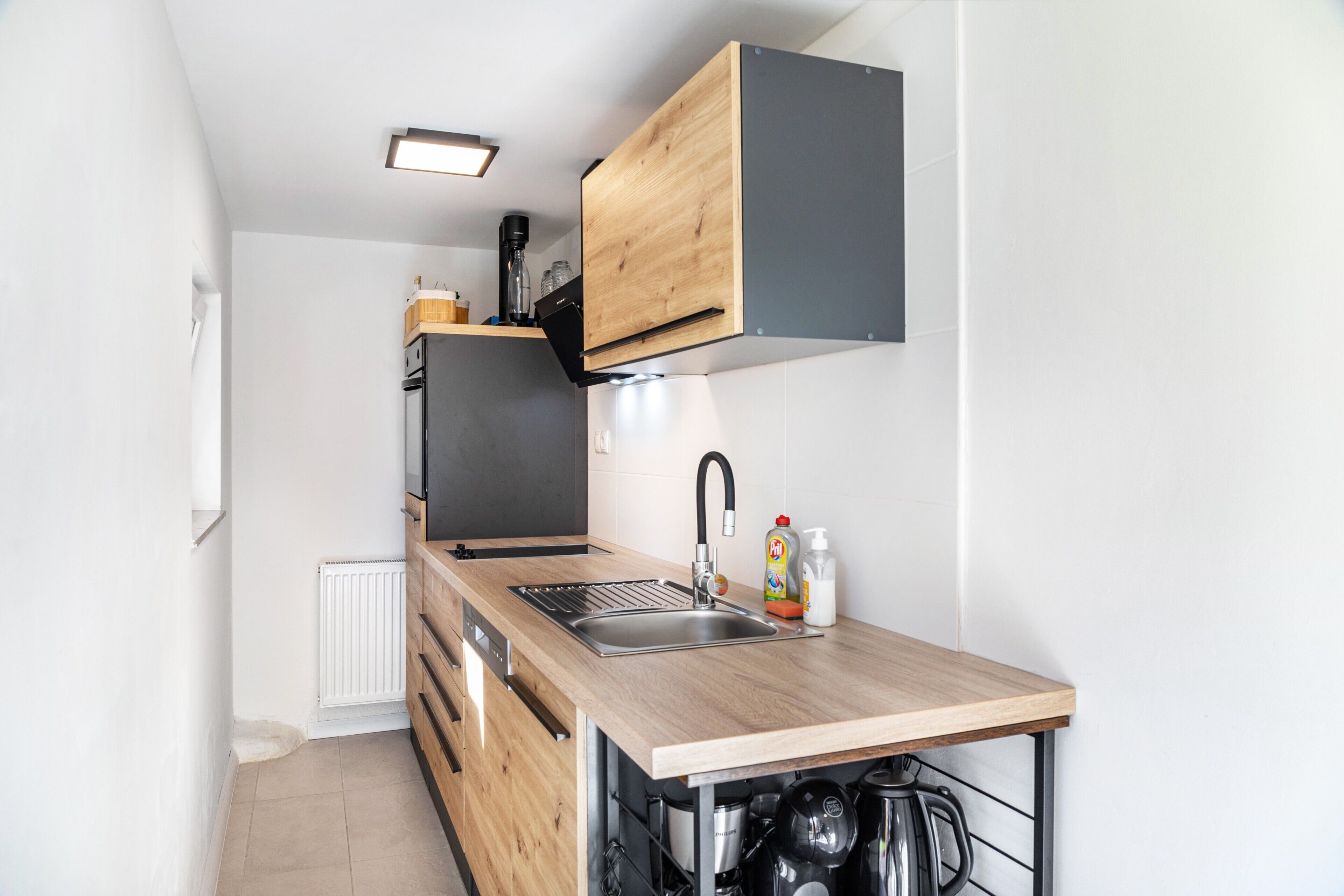 A compact kitchen with a wooden countertop, a built-in sink, and a black range hood.