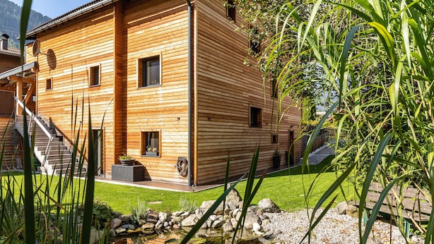 Una cabaña de madera con un sendero de piedra que lleva a la entrada, un pequeño estanque con lirios y un patio cubierto de césped.