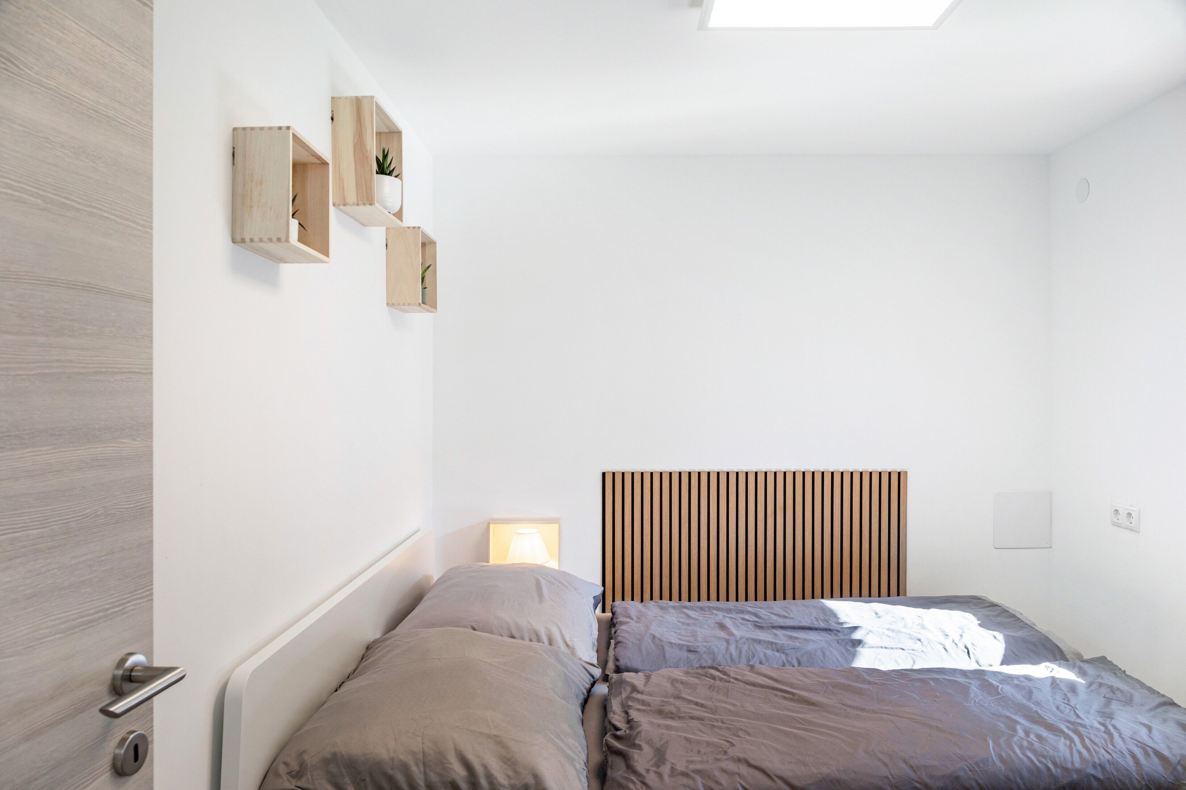 Ein Schlafzimmer mit einem Bett, einem Nachttisch, einem an der Wand befestigten Regal mit einer Pflanze und einem Fenster.