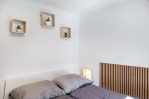 Une chambre à coucher avec un lit, une lampe de chevet et trois étagères fixées au mur, sur lesquelles sont disposées des plantes.