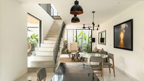 A modern dining area with a glass table, multiple chairs, a staircase, and a large framed picture on the wall. - Melasti Villa 2 by Alfred in Bali (Canggu)
