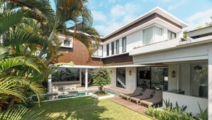 A modern two-story house with a swimming pool, outdoor seating, and lush greenery. - Melasti Villa 2 by Alfred in Bali (Canggu)