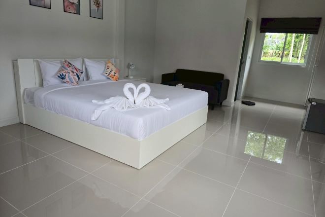 A modern hotel room with a large bed, white bedding, and a heart-shaped towel decoration.