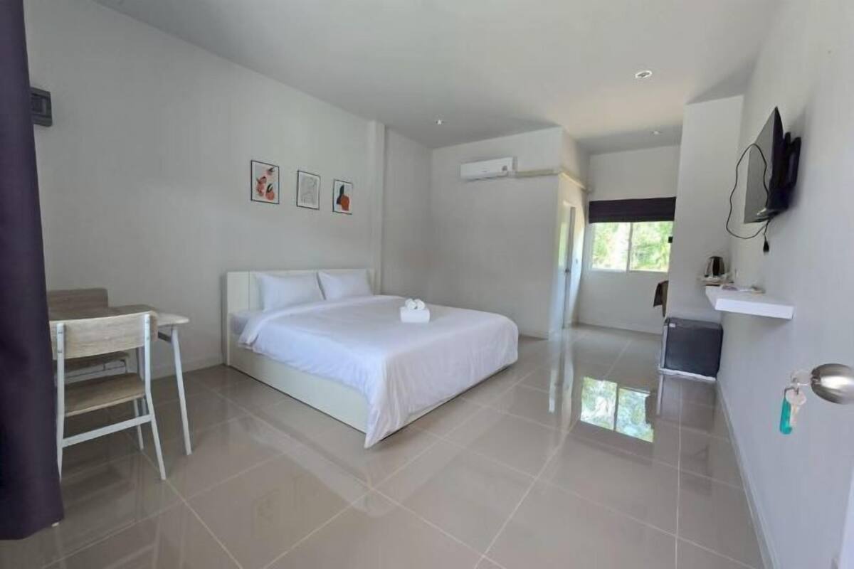 A modern hotel room with a bed, a desk, a TV, and a shower area.
