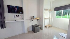 A modern room with a flat-screen TV mounted on the wall, a small refrigerator, a shelf with items, and a window with a view of greenery. - Wae Phak Stay Hostel@Khok Kloi (Takua Thung)