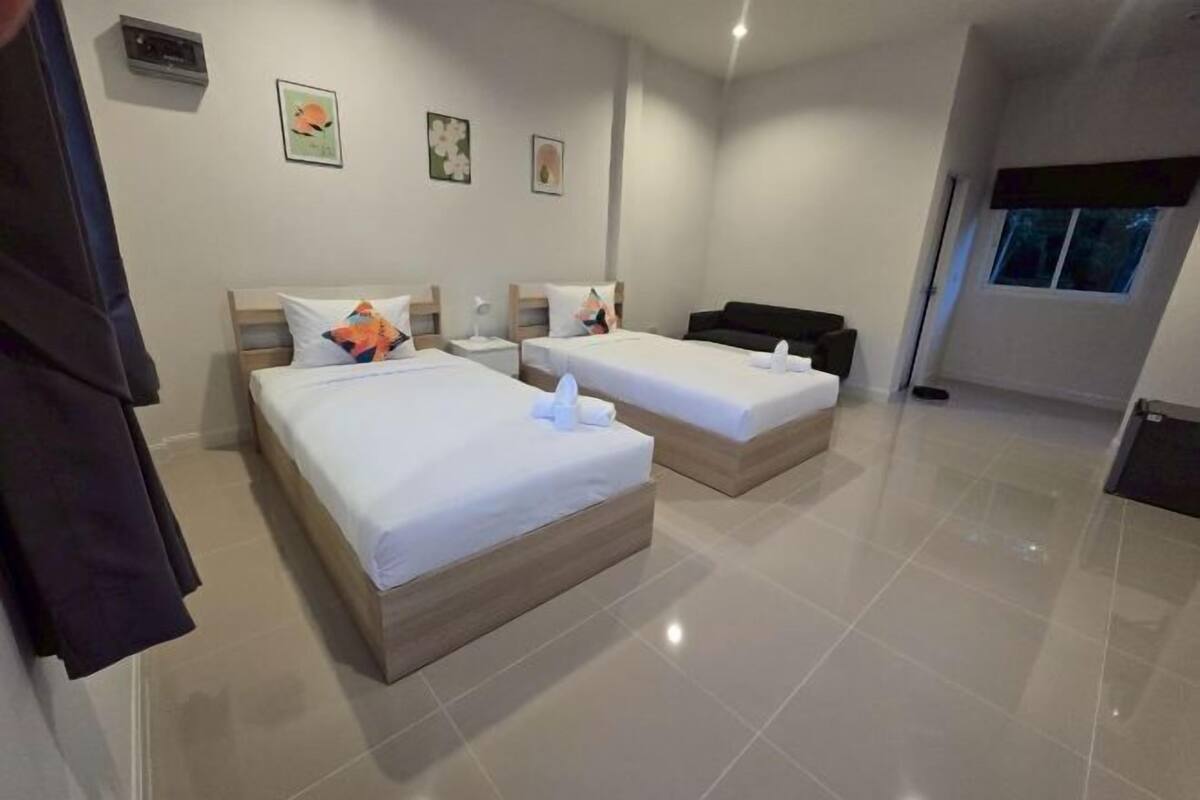 A hotel room with two beds, a sofa, a window, and artwork on the wall.