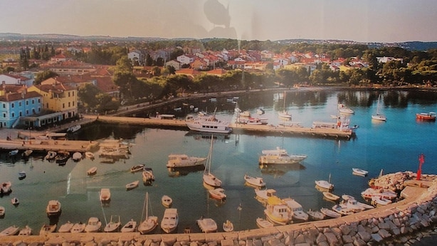 A harbor with boats docked, a stone quay, and buildings in the background. - Apartments Villa Dina (Fazana)