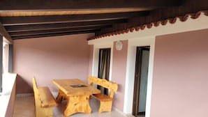 A wooden table and benches in a covered outdoor area with tiled flooring and a pink wall. - Apartments Villa Dina (Fazana)