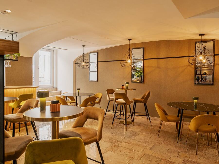A modern interior with round tables and yellow chairs, a bar area with bottles, and decorative wall mirrors.