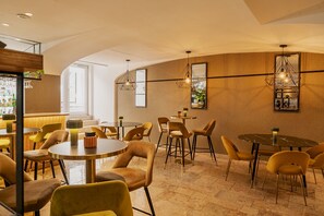 Un interior moderno con mesas redondas y sillas amarillas, una zona de bar con botellas y espejos decorativos en la pared.