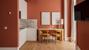 Eine kleine Küche mit Marmorarbeitsplatte, zwei gerahmten Kunstwerken, einem Holztisch mit gelben Stühlen und einem Fernseher an der Wand.