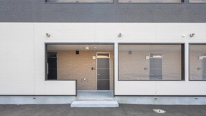 A modern building with a flat facade, a central entrance with steps, and large windows on the right side. - CHARMANT 1B (Minamifurano)