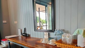 A room with a wooden desk, a mirror, a kettle, water bottles, a fan, and a tray with snacks. - Rimwang The River Life (Sai Yok)
