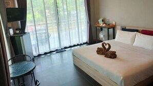 A hotel room with a bed, a desk, a chair, a TV, a fan, and a view of the outdoors. - Rimwang The River Life (Sai Yok)