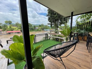 A balcony with a view of a river, surrounded by greenery and a wooden deck. - Rimwang The River Life (Sai Yok)