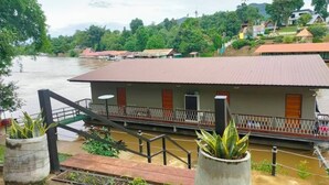 A riverside building with a balcony, a staircase leading to the entrance, and a view of the river and surrounding greenery. - Rimwang The River Life (Sai Yok)