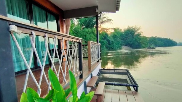 A wooden deck with a railing overlooking a calm river, surrounded by greenery. - Rimwang The River Life (Sai Yok)