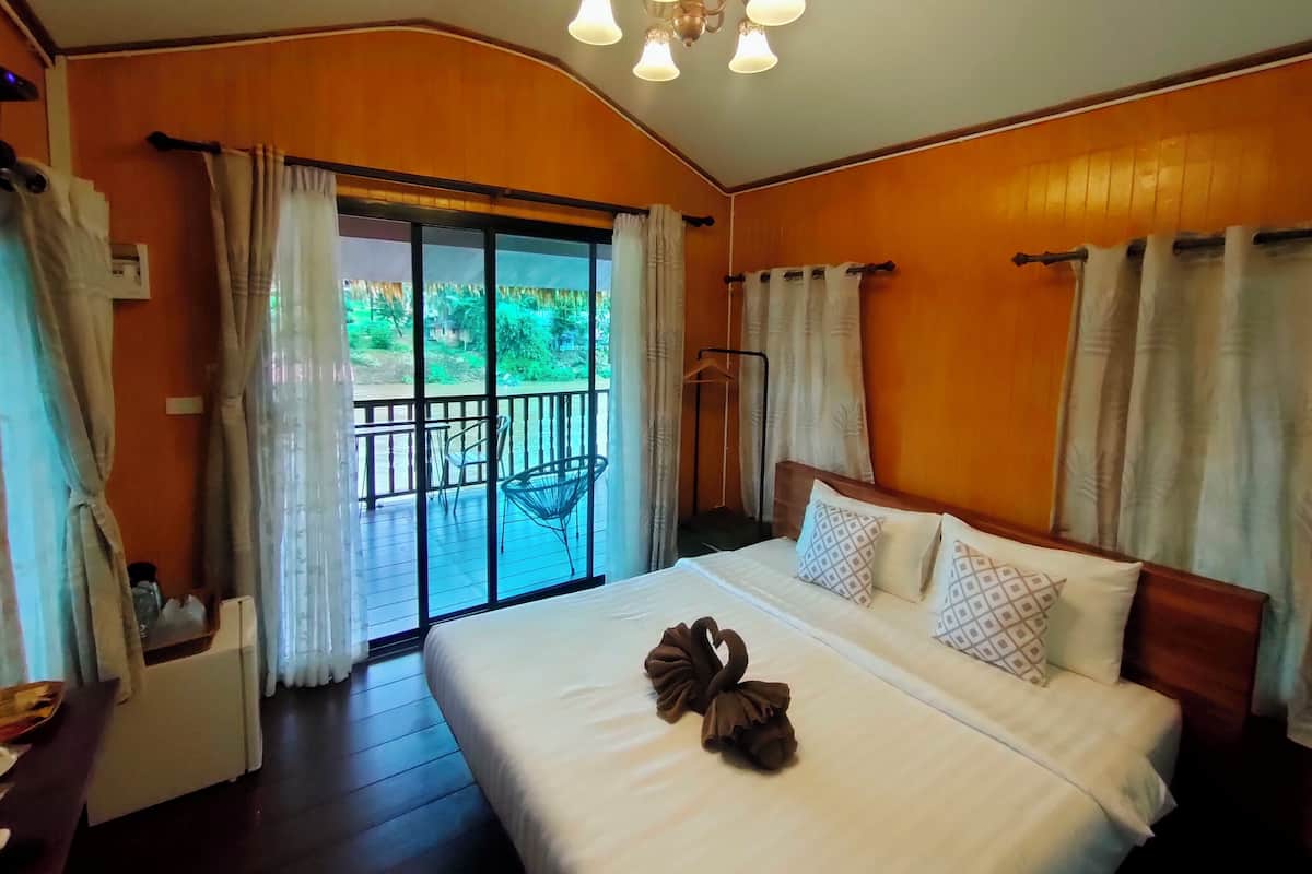 A hotel room with a large bed, a balcony with a view of greenery, and a ceiling light fixture.
