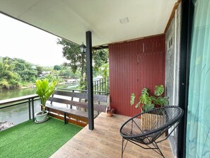 A balcony with a wooden floor, a black chair, and a potted plant. - Rimwang The River Life (Sai Yok)