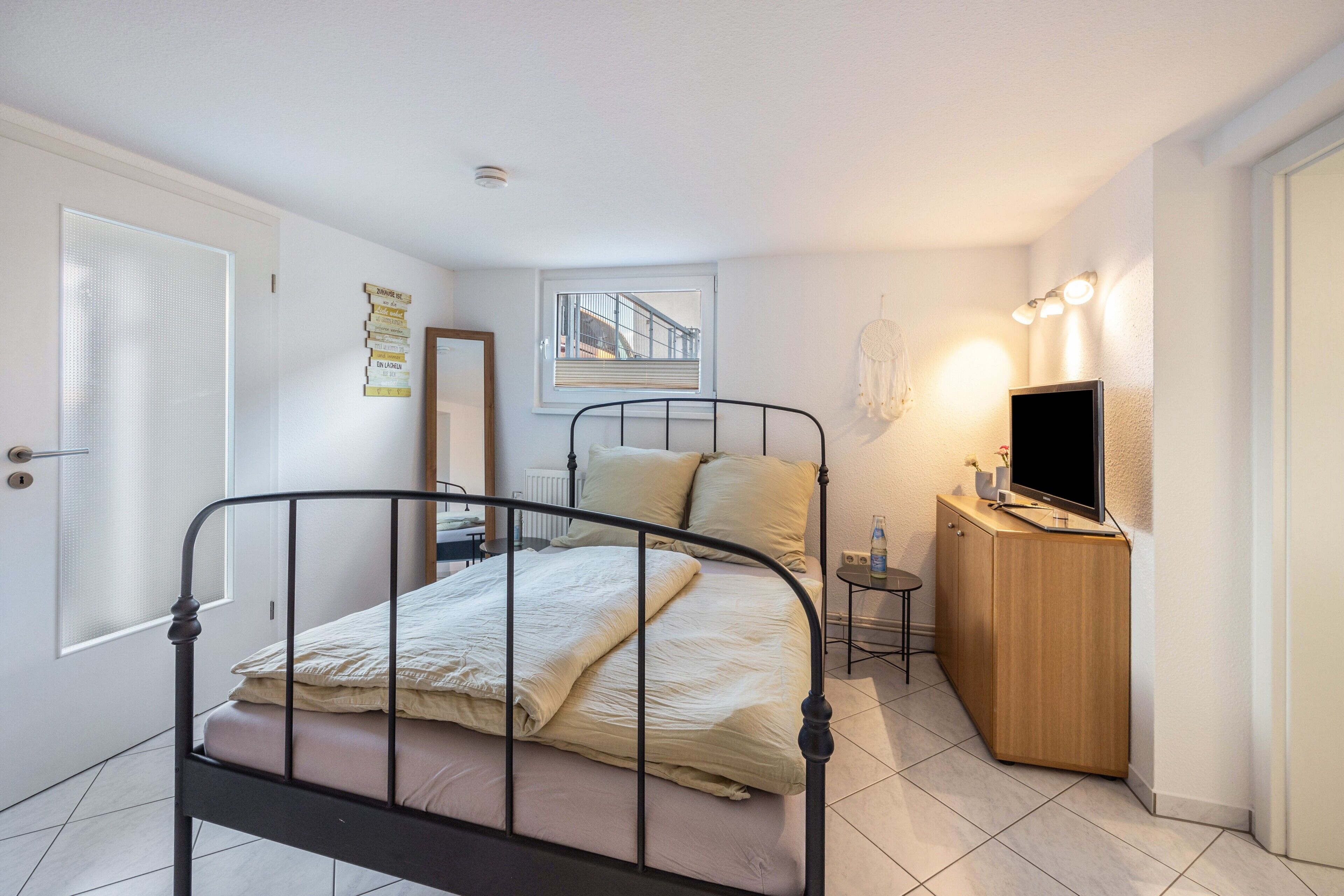 Une chambre à coucher avec un lit, une télévision, une petite table, une armoire, une fenêtre et une porte.
