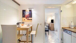 Une cuisine moderne avec un coin repas, un tableau accroché au mur et une vue sur la chambre adjacente.