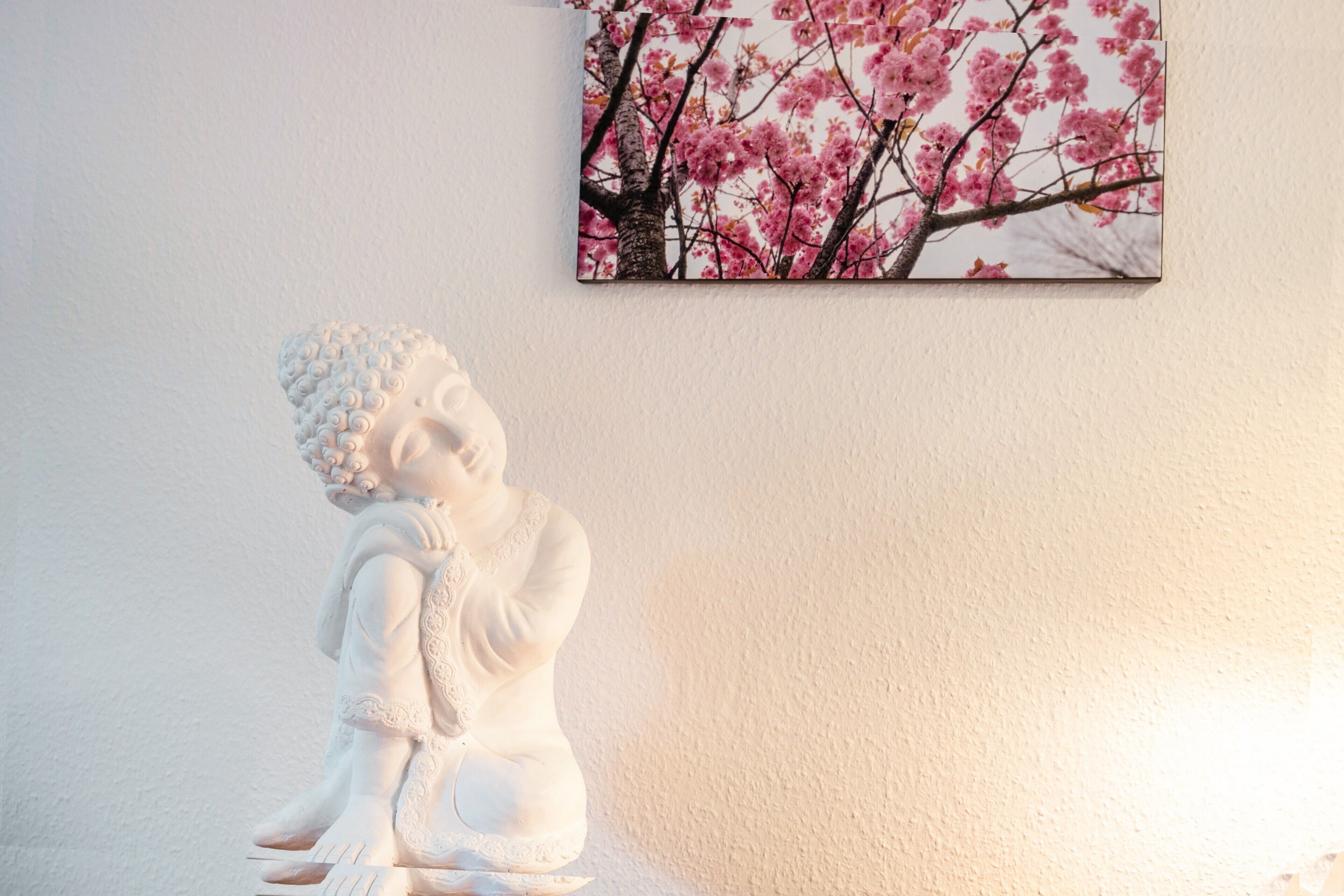 Una estatua de una figura sentada, un cuadro con flores de cerezo y una pared con textura.