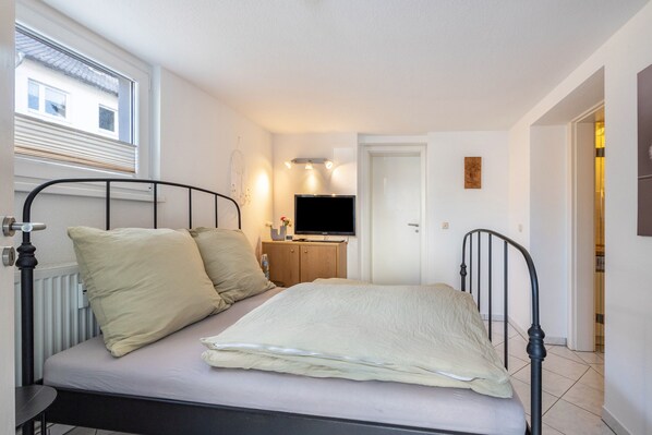 A bedroom with a bed, a television, a radiator, and a window.
