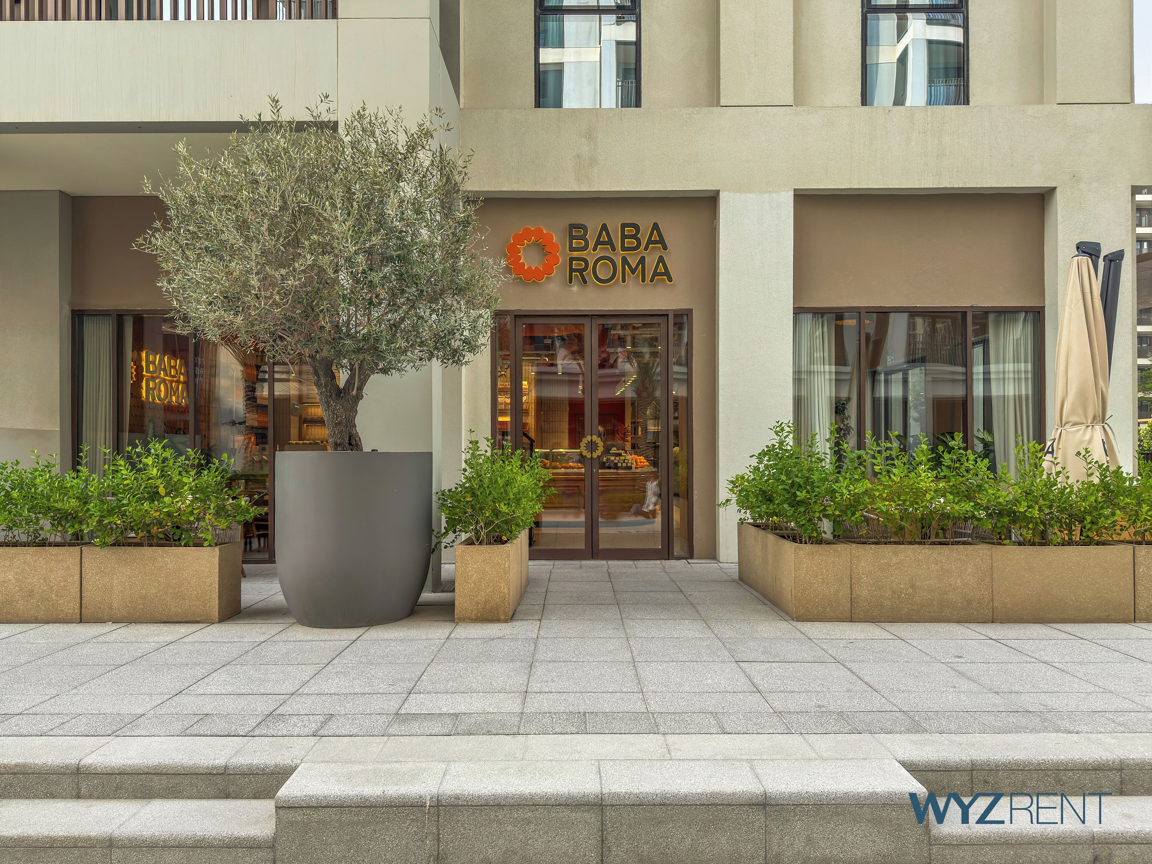 Un bâtiment portant une enseigne « BABA ROMA », avec des plantes en pot et le logo « WYZRENT ».