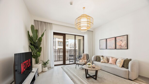 A modern living room with a flat-screen TV, a sofa, a coffee table, and a large potted plant. - WYZ RENT|Beachside 2BR W Pool Gym Lagoon Access (Dubai)