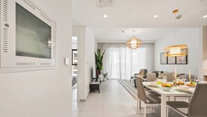 A modern dining area with a white table, chairs, and a chandelier. - WYZ RENT|Beachside 2BR W Pool Gym Lagoon Access (Dubai)