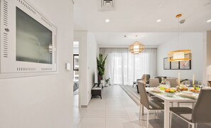 A modern dining area with a white table, chairs, and a chandelier. - WYZ RENT|Beachside 2BR W Pool Gym Lagoon Access (Dubai)