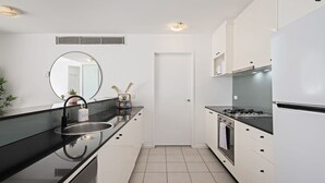 Une cuisine moderne avec un plan de travail noir, des meubles blancs, un évier en acier inoxydable et une cuisinière.
