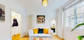 Una sala de estar moderna con un sofá blanco, cojines coloridos, una mesa de centro de madera y un ventanal grande.