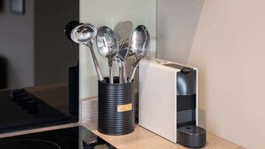 A kitchen area with a stove, a black utensil holder with various kitchen tools, and a white appliance. - Modern 1BR Central Liverpool Apt with WiFi (Merseyside)